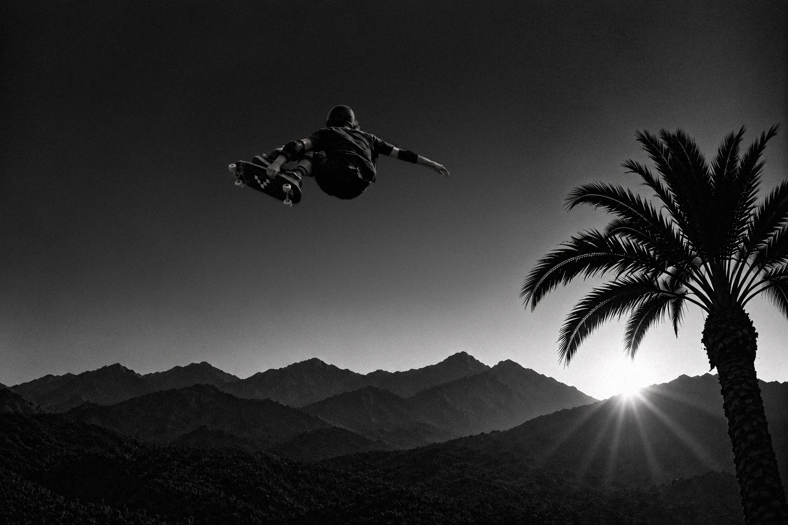Skateboarder airborne above palm trees and desert mountains at sunset.
